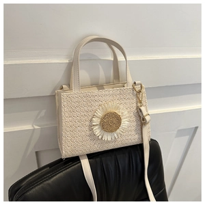 Detail view of woven straw handbag featuring a white daisy flower and thin shoulder strap