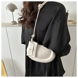 Detail view of white crescent bag with knot strap and gold snap button on a black outfit