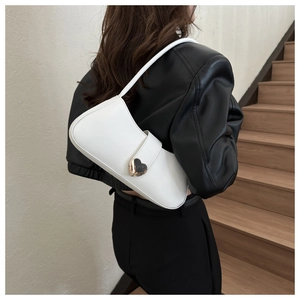 Close-up of white crescent shoulder bag with a gold heart buckle on a model wearing black