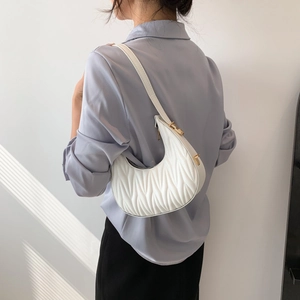 Minimalist white pleated crescent shoulder bag with gold hardware shown on a model