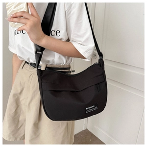 Detail of black crossbody bag with adjustable wide strap and white brand label