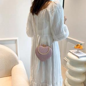 Pink glitter heart-shaped crossbody bag with gold chain strap worn by a woman