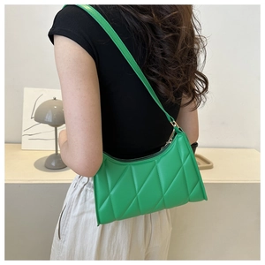 Detail of green quilted baguette bag with diamond stitching shown on model's shoulder