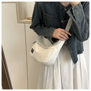 Minimalist cream crossbody bag with black logo patch and wide strap on model
