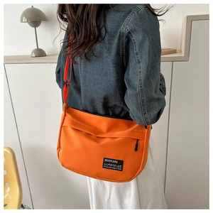 Detail of vibrant orange crossbody bag with adjustable strap worn in a lifestyle setting