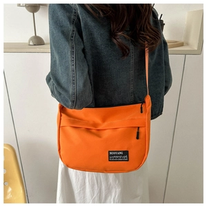 Close-up of bright orange canvas crossbody bag with adjustable strap and logo detail