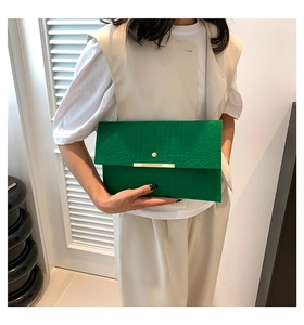 Détail d'une pochette enveloppe verte à texture crocodile avec fermoir doré sur modèle