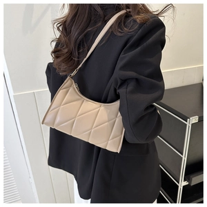 Detail showing beige quilted shoulder bag with large diamond stitching on a model