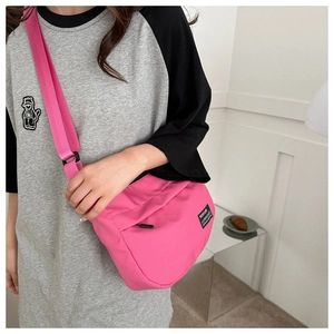 Detail of bright pink crossbody bag with wide nylon strap and front zipper pocket