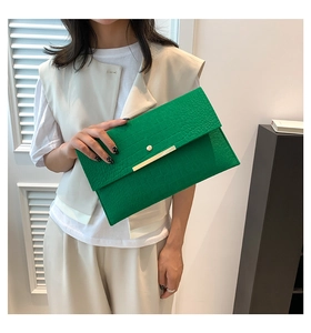 Détail de la texture croco verte et boucle en métal doré sur une pochette enveloppe chic