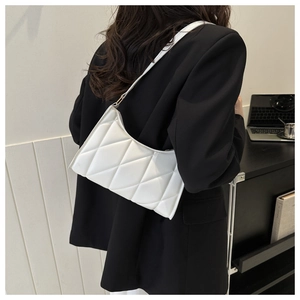 Detail of white quilted baguette bag with diamond pattern and leather strap on shoulder
