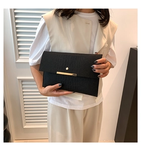 Détail de la pochette enveloppe noire texture crocodile avec barre métallique dorée chic