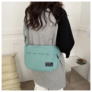 Detail view of mint green canvas messenger bag worn crossbody in minimalist interior