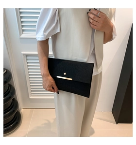 Détail d'une pochette enveloppe noire à motif crocodile avec fermoir en métal doré