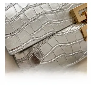 Detail of silver crocodile-embossed envelope bag with golden metallic clasp closure