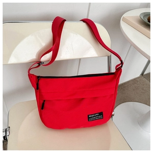 Detail view of red canvas crossbody bag with adjustable strap and brand logo tag
