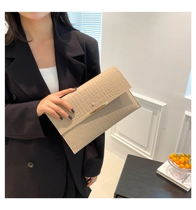 Détail de la pochette enveloppe beige à motif crocodile et barre dorée élégante