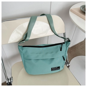 Detail of mint green nylon crossbody bag showing broad strap on a minimalist chair