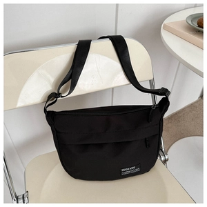 Detail view of black canvas crossbody bag with brand logo tag on a white chair