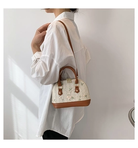 Detail of floral embroidery and brown leather trim on a beige woven shell-shaped bag