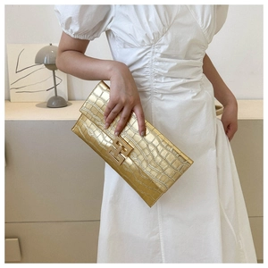 Close-up of golden envelope clutch featuring crocodile pattern and H-shaped metal buckle
