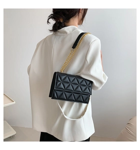 Detail der schwarzen Stepptasche mit goldener Kette, getragen von Model in Weiß