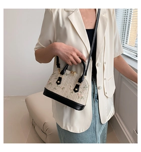 Detailed side view of straw shell bag with floral embroidery worn by a model