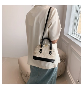 Detail view of woven shell bag with floral embroidery and black leather straps