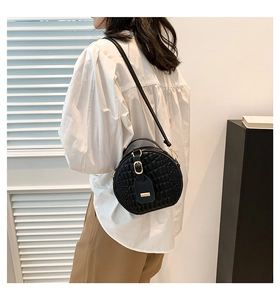 Detail of black round crossbody bag with crocodile texture and gold hardware on model