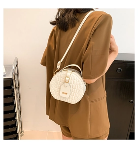 Detail of white round crossbody bag with quilted texture and gold hardware on model