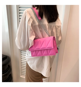 Detail of bright pink quilted crossbody bag with silver chain strap on model outfit