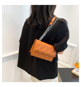 Close-up of orange quilted crossbody bag with silver chain strap and triangle stitching