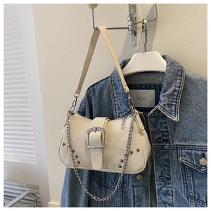 Close-up of beige canvas shoulder bag with silver buckle, rivets, and metal chain detail