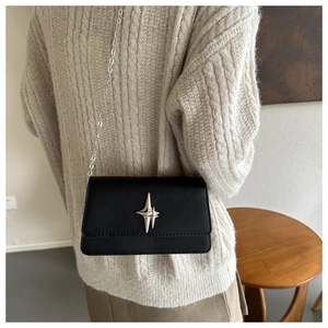Detail view of black crossbody bag with silver star ornament and metal chain strap