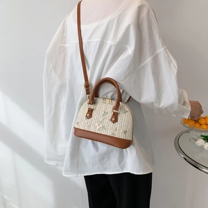 Women's woven shell bag with floral embroidery and brown leather trim worn by a model