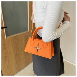 Detail of bright orange trapezoid handbag featuring a silver star buckle and shoulder strap