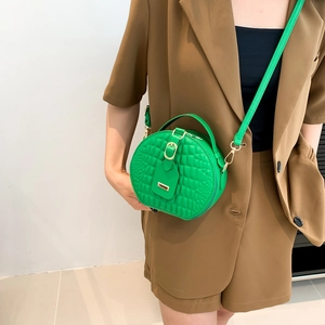 Minimalist green round crossbody bag with crocodile texture and golden buckle on model