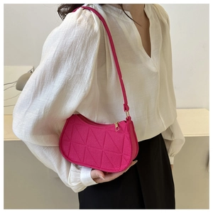 Close-up of a stylish fuchsia quilted underarm bag with triangle pattern worn by model