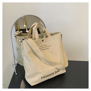 Detail of beige canvas tote bag with adjustable strap and metal snap closure
