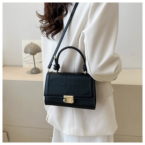 Detail of black crossbody bag featuring crocodile texture and gold metal buckle on white suit