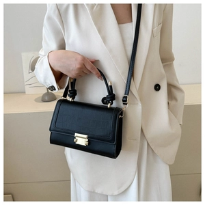 Detail of black crocodile texture small square bag worn with a white blazer