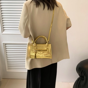 Golden metallic mini handbag with crocodile texture and tassel detail on model