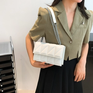 White quilted rectangular chain bag with geometric texture worn by a model in green blazer