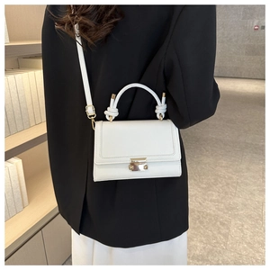 White structured crossbody bag with knotted handle detail shown in a lifestyle indoor setting
