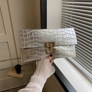 Dettaglio della borsa clutch argento con motivo coccodrillo e fibbia dorata in mano