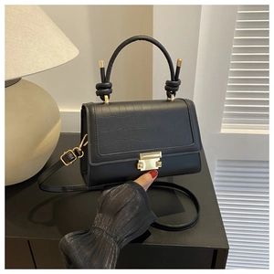 Detail of black faux crocodile leather flap and gold buckle on a stylish crossbody bag