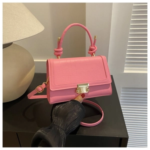 Detail of pink crocodile pattern handbag featuring a decorative knot handle and gold clasp