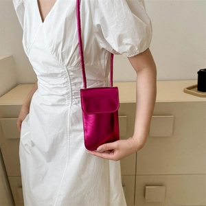Bolso bandolera mini rojo rosa metálico para móvil sobre un vestido blanco elegante