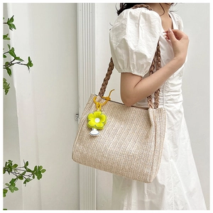 Detail of straw woven tote bag with brown braided handles and yellow flower charm