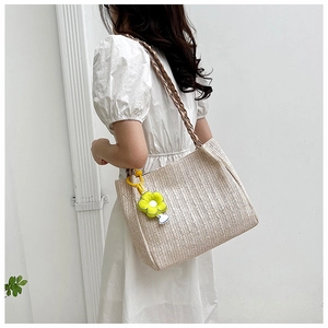 Detail of beige woven tote bag with brown straps and a yellow flower pendant charm